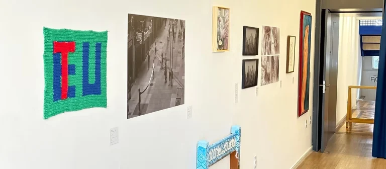 Corredor de exposição de artes visuais com quadros e tapeçaria no espaço cultural Momento D'Artes